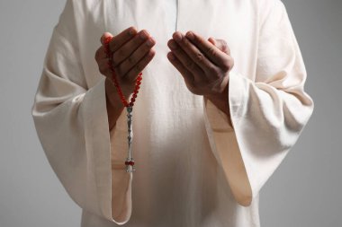 Misbaha 'lı Müslüman bir kadın açık gri arka planda dua ediyor, yakın plan