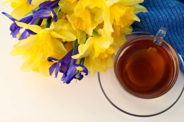 Bir fincan aromatik çay, güzel sarı nergis çiçeği beyaz masada, düz yerde.