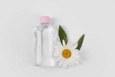 Beyaz arka planda bebek yağı ve çiçekli şeffaf şişe, düz yatıyordu.