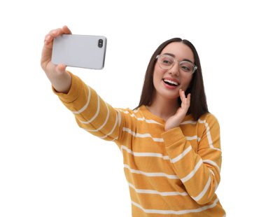 Gülümseyen genç bir kadın beyaz arka planda akıllı telefonuyla selfie çekiyor.