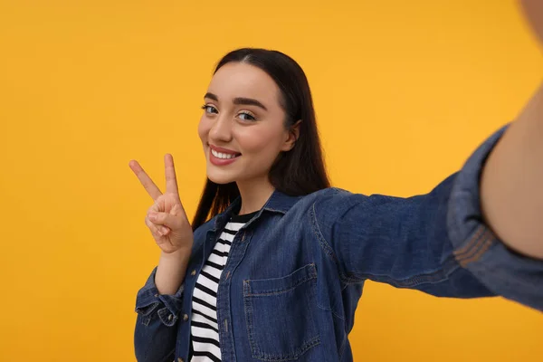 Uśmiechnięta Młoda Kobieta Robi Selfie Pokazuje Znak Pokoju Żółtym Tle — Zdjęcie stockowe