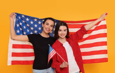 4 Temmuz - ABD 'nin Bağımsızlık Günü. Sarı arka planda Amerikan bayrakları olan mutlu kadın ve kızı