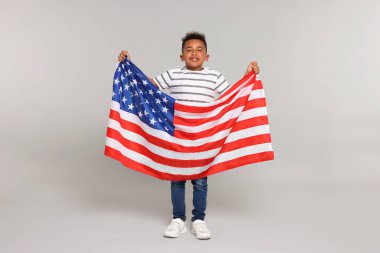 4 Temmuz - ABD 'nin Bağımsızlık Günü. Açık gri arka planda Amerikan bayrağı taşıyan mutlu çocuk.