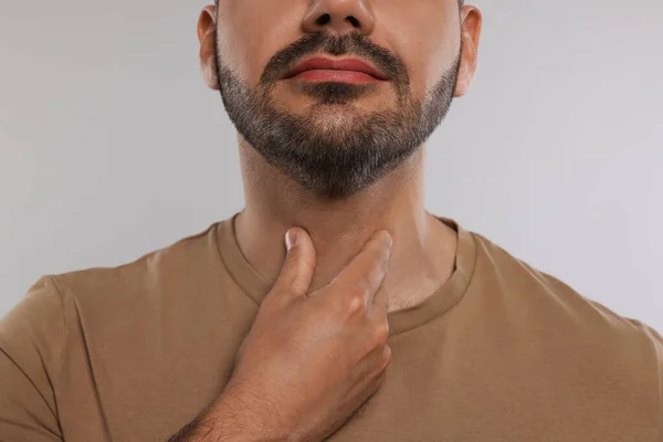 内分泌系 軽い灰色の背景で甲状腺自己検査をしてる男が近づいてる — ストック写真