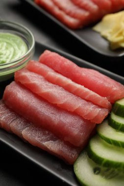 Lezzetli sashimi (taze çiğ ton balığı parçaları) ve siyah tabakta salatalık dilimleri, yakın plan