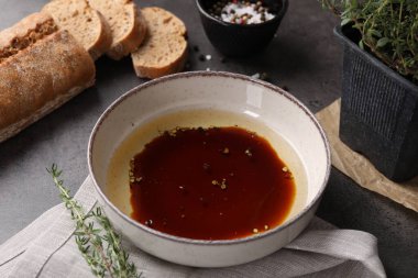 Koyu gri masada bir kase balzamik sirke, yağ, baharat ve ekmek.