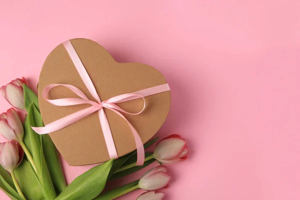 stock image Heart shaped gift box with bow and beautiful tulips on pale pink background, flat lay. Space for text