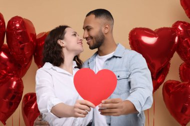 Lovely couple with red paper heart on beige background. Valentine's day celebration