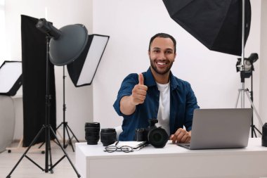 Modern fotoğraf stüdyosunda genç profesyonel fotoğrafçı baş parmağını kaldırıyor.