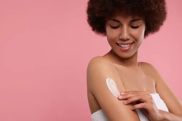 stock image Beautiful young woman applying body cream onto arm on pink background, space for text