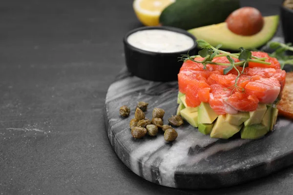 stock image Delicious salmon tartare served with avocado and sauce on dark table, closeup. Space for text