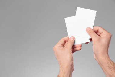 Man holding paper cards on grey background, closeup. Mockup for design