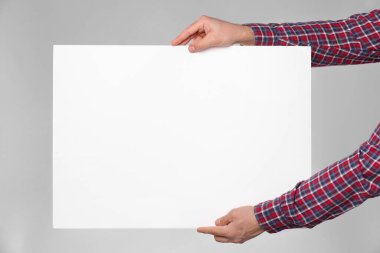 Man holding sheet of paper on grey background, closeup. Mockup for design