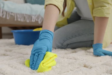 Lastik eldivenli bir kadın, içeride paçavrayla halı temizliyor, yakın plan. Metin için boşluk