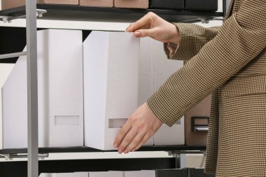 Woman taking folder with documents from shelf in office, closeup
