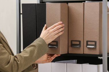 Woman taking folder with documents from shelf in office, closeup