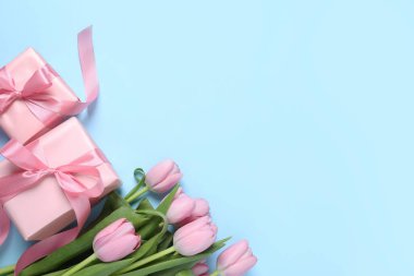 Güzel hediye kutuları ve açık mavi arka planda pembe lale çiçekleri. Metin için boşluk