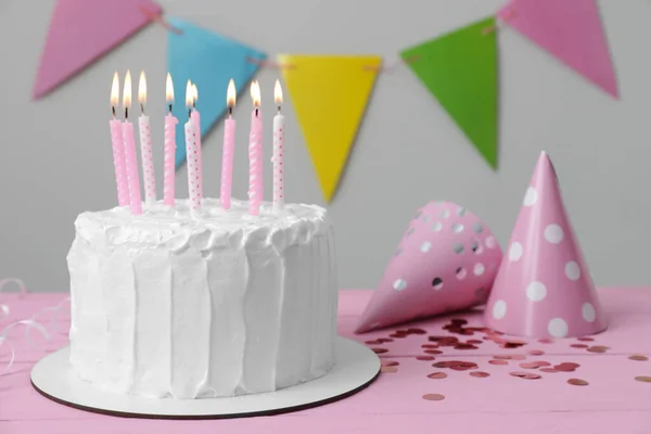 美味的蛋糕 有燃烧的蜡烛和粉色木制桌子上的派对帽 案文的篇幅 — 图库照片