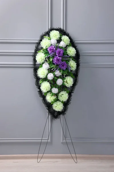 stock image Funeral wreath of plastic flowers near light grey wall indoors