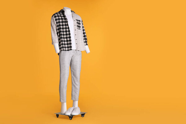 Male mannequin with sneakers dressed in white t-shirt, stylish checkered shirt and pants on orange background. Space for text