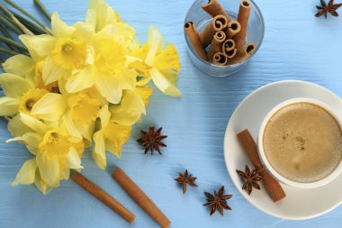 Güzel sarı nergisler, bir fincan kahve, tarçın çubukları ve açık mavi ahşap masa üzerinde anason yıldızları.