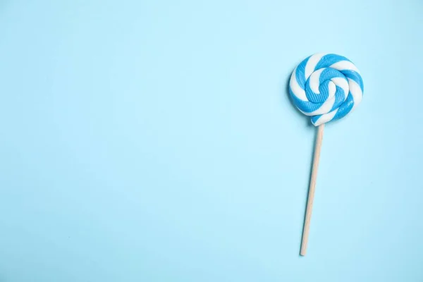 Stick with bright lollipop on light blue background, top view. Space for text