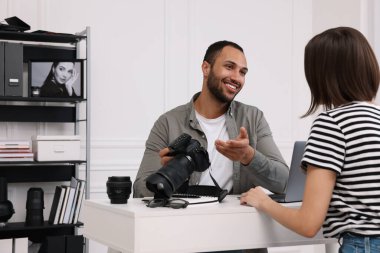 Modern fotoğraf stüdyosunda bir kadınla konuşurken elinde kamera olan genç profesyonel fotoğrafçı.