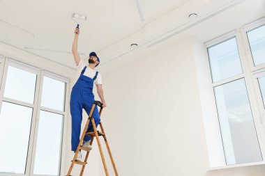 Üniformalı işçiler tavanı merdivenle boyuyor. Kapalı alanda, düşük açılı.