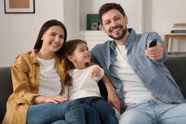 Evde film izleyen mutlu bir aile. Babam uzaktan kumandayla televizyon kanallarını değiştiriyor.