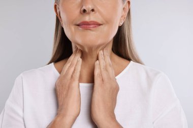 Endocrine system. Senior woman doing thyroid self examination on light grey background, closeup clipart