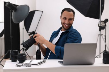 Modern fotoğraf stüdyosunda dizüstü bilgisayarda çalışan genç profesyonel fotoğrafçı.