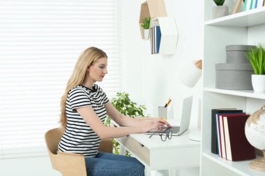 Home workplace. Woman working on laptop at white desk in room