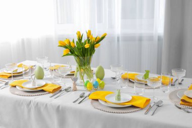 Festive table setting with glasses, painted eggs and vase of tulips. Easter celebration