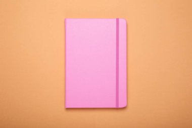 Soluk turuncu arka planda kapalı pembe ofis defteri, üst görünüm