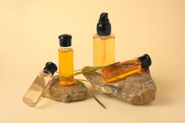 Kozmetik ürünleri olan şişeler, bej arka planda taşlar ve sazlıklar