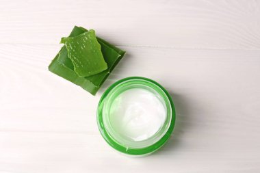 Kozmetik krem kavanozu ve beyaz ahşap masa üzerindeki aloe vera yapraklarını kes.