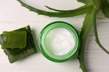 Kozmetik jel kavanozu ve aloe vera yaprakları beyaz ahşap masada, düz yatıyordu.
