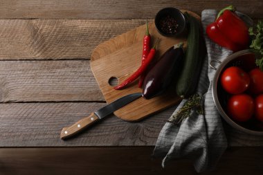 Ratatouille pişiriyorum. Sebzeler, biberler, otlar ve bıçaklar ahşap masada, düzlük ve metin için yer var.