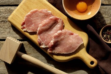 Şnitzel pişiriyorum. Çiğ domuz eti dilimleri, yumurta, biber ve ahşap masa üzerinde et yumuşatıcısı.