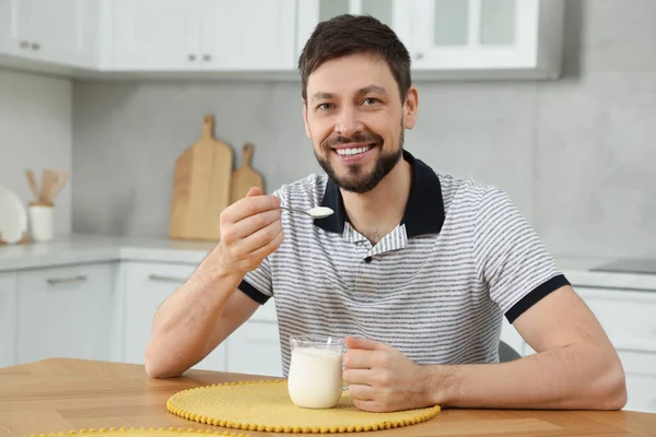 一个英俊的男人在厨房的桌子上端着美味的酸奶 — 图库照片
