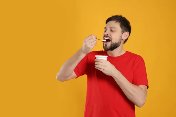 一个英俊的男人在橙色背景下吃着美味的酸奶 — 图库照片