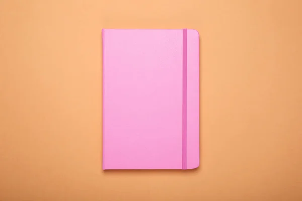 浅橙色背景的闭合粉色办公室笔记本 顶部视图 — 图库照片