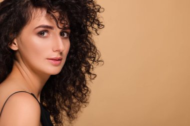 Bej arka planda uzun kıvırcık saçlı güzel bir genç kadın. Metin için boşluk