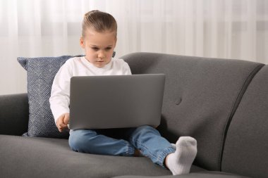 Evdeki kanepede dizüstü bilgisayar kullanan küçük bir kız. İnternet bağımlılığı