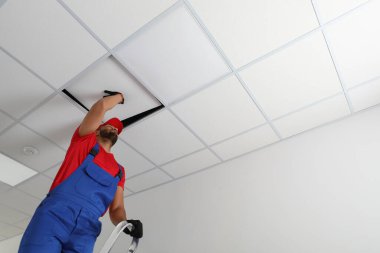 Electrician repairing ceiling light indoors, low angle view. Space for text