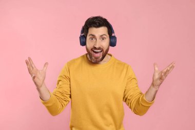 Duygusal adam pembe arka planda kulaklıkla müzik dinliyor.