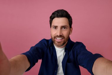Gülümseyen adam pembe arka planda selfie çekiyor.