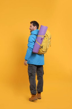 Sırt çantalı bir adam turuncu arka planda yürüyor. Etkin turizm