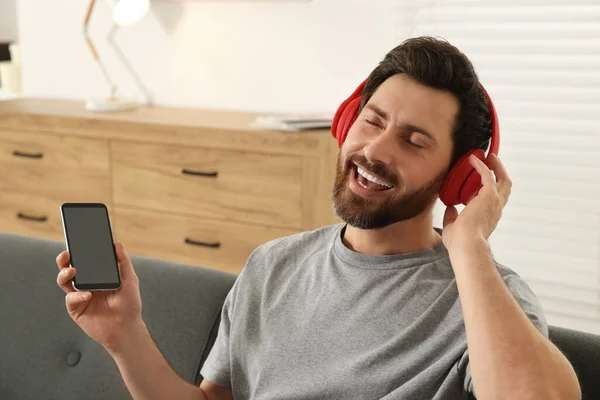 stock image Happy man listening music with headphones on sofa indoors