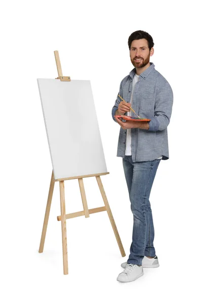 stock image Happy man with brush and artist`s palette near easel with canvas against white background. Creative hobby